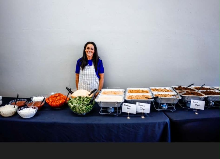Jeannette behind a Cater It taco bar with taco meat, rice, Rotel dip and toppings